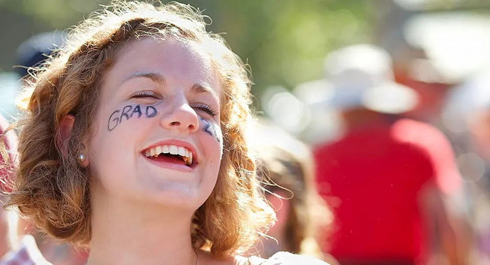 Una giovane donna con i capelli ricci e la scritta GRAD sul viso festeggia la sua cerimonia di diploma alla Gulf Islands Secondary School.