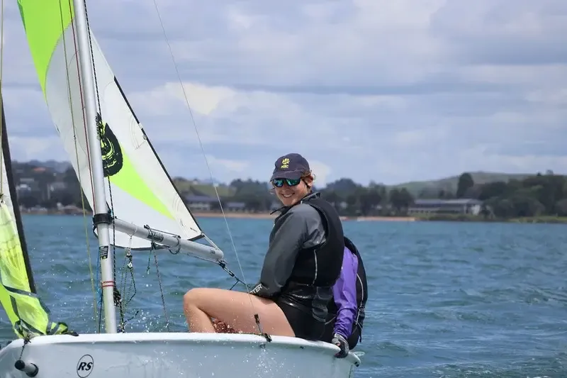 Chica sonriendo mientras gobierna un pequeño velero cerca de la costa