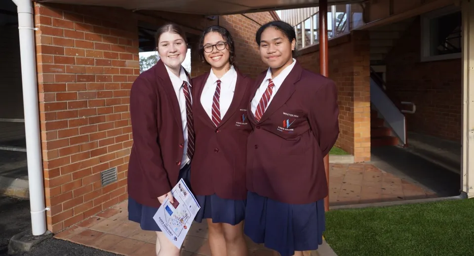 Tre studenti del Whites Hill State College sono insieme nel corridoio e tengono un cartello.