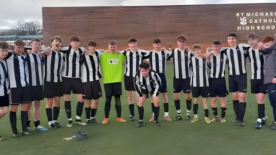 Un gruppo di studenti e studentesse della St. Michael Catholic Secondary School con maglie a strisce bianche e nere si trova su un campo sportivo davanti all'edificio scolastico.