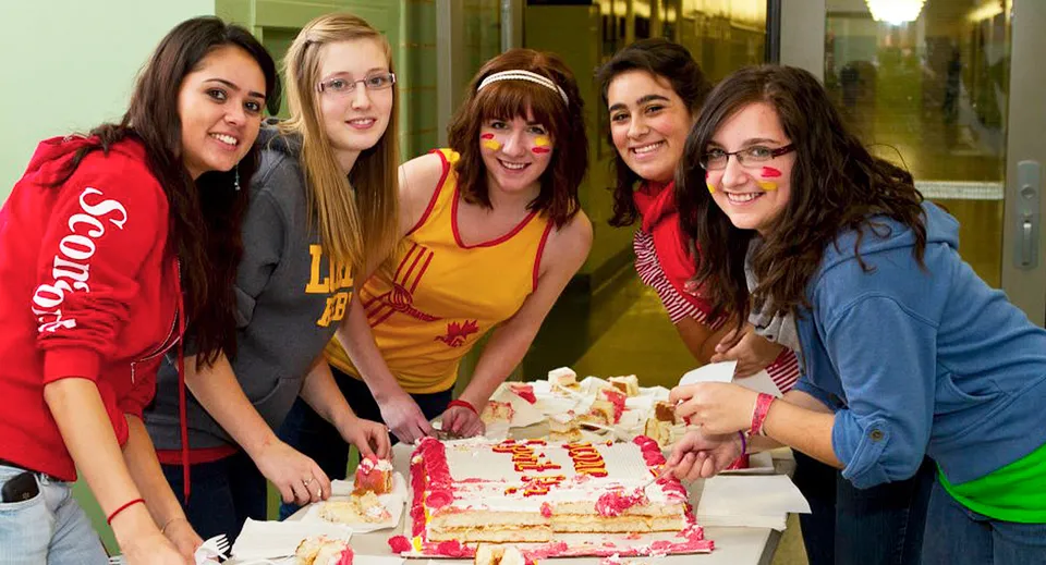 Un gruppo di studentesse della Strathcona High School festeggia insieme al chiuso con una torta di compleanno.