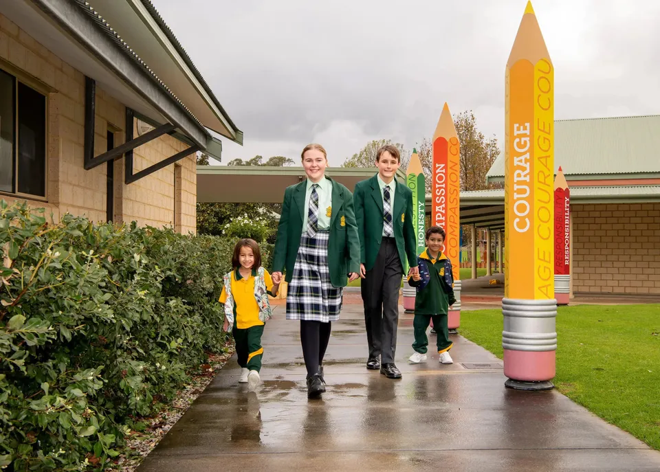 Quattro studenti della Frederick Irwin Anglican School in divisa scolastica camminano lungo un viale accanto a grandi sculture a forma di matita.