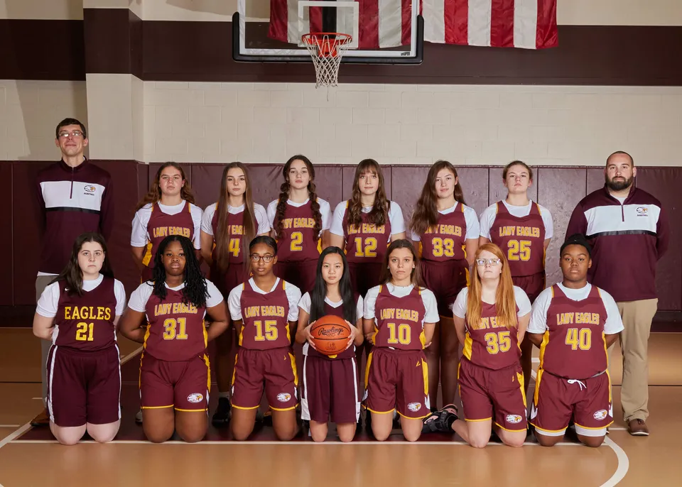 Un gruppo di studentesse della Liberty Christian Academy posa in divisa da basket nella palestra davanti al canestro.