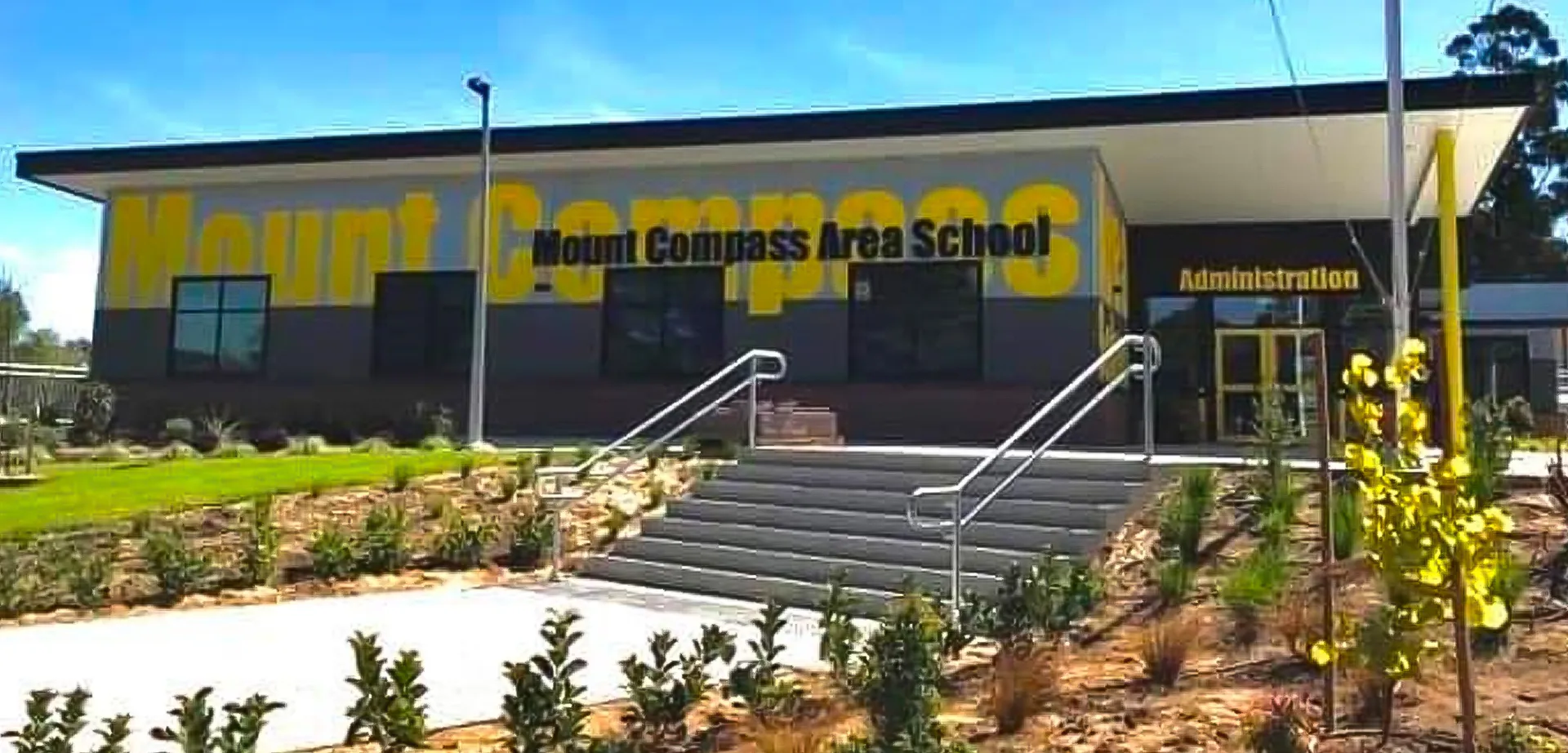 Si vede l'edificio della Mount Compass Area School con una grande insegna gialla e una scalinata che porta all'ingresso.