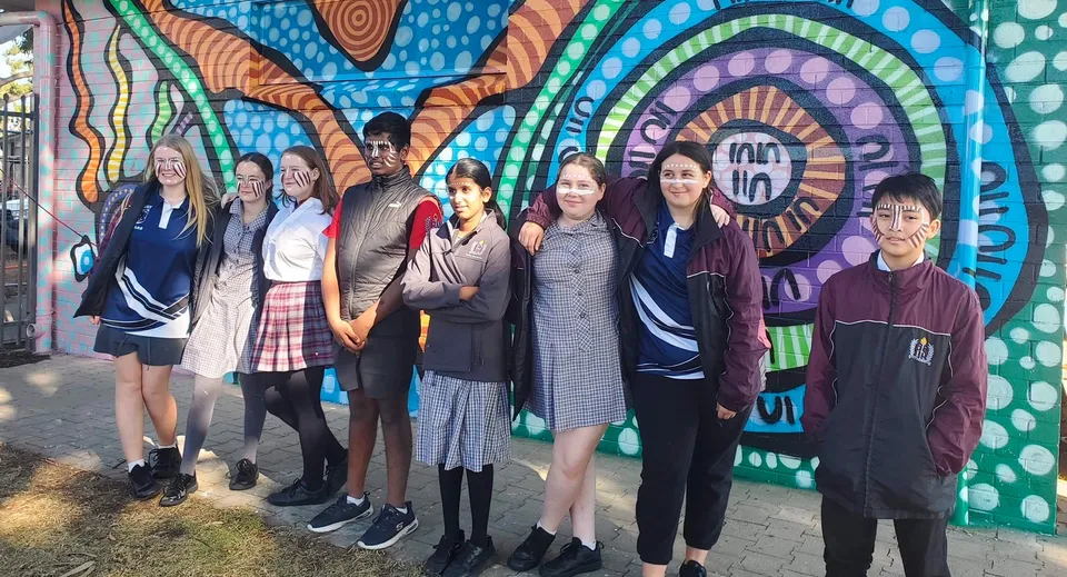Studenti della Findon High School in piedi davanti a un murale colorato con motivi geometrici.