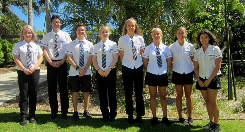 Un gruppo di studenti in divisa scolastica si trova in un ambiente tropicale all'interno del campus della Yeppoon State High School.