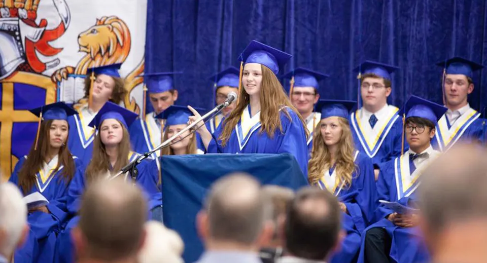 I diplomati e le diplomate della Prairie Christian Academy sono sul palco in toga blu davanti a una tenda blu.