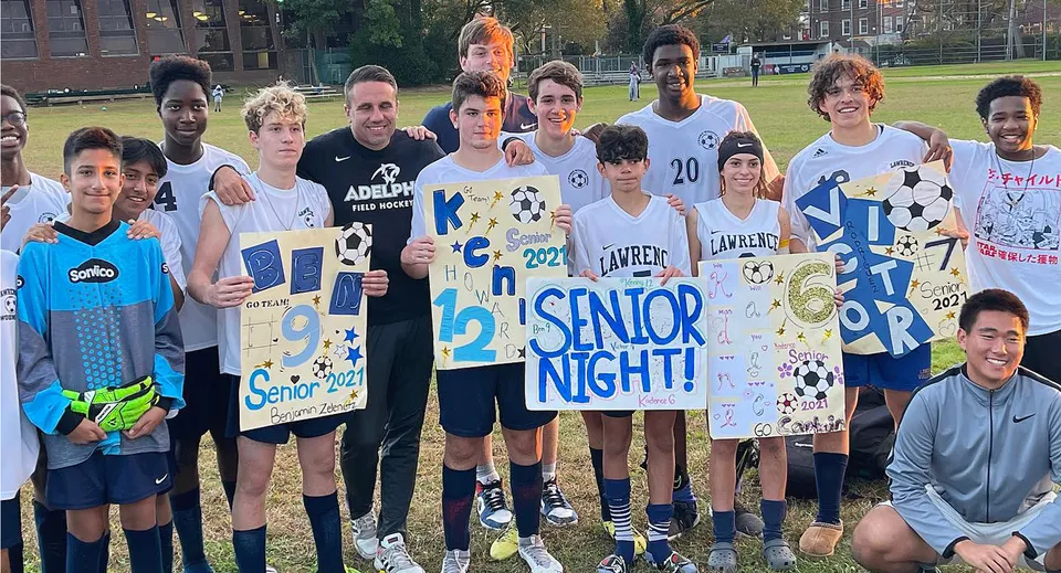 Un gruppo di studenti festeggia la Senior Night sul prato della Lawrence Woodmere Academy tenendo dei cartelli in mano.