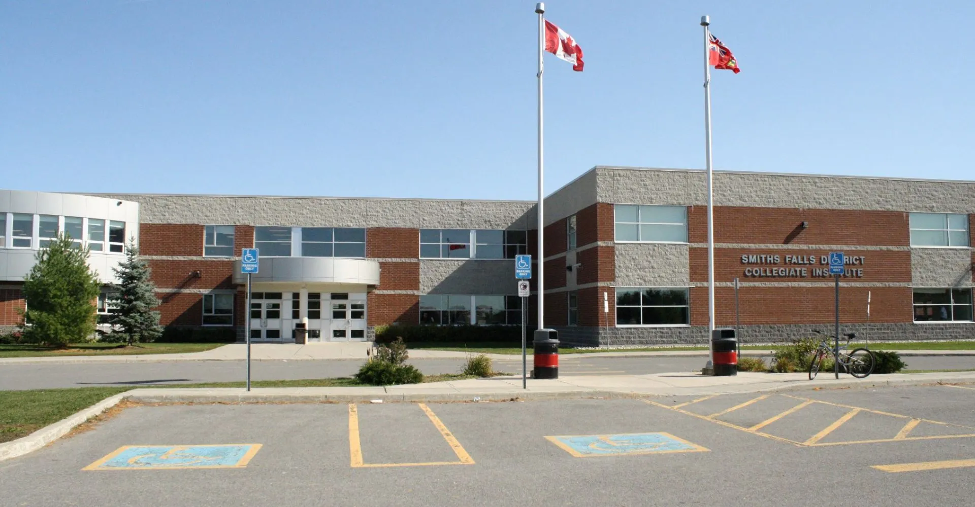 L'edificio moderno a più piani con bandiere canadesi del Smiths Falls District Collegiate Institute è circondato da un parcheggio con posti riservati ai disabili.