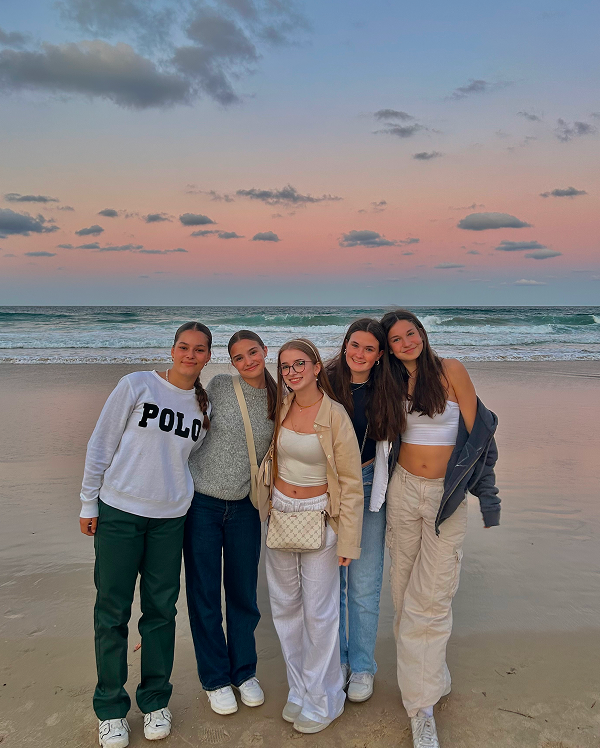 Cinco estudiantes posando juntas en la playa al atardecer