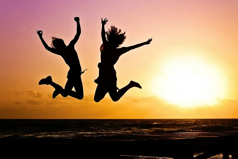 Silhouetten von zwei Personen, die bei Sonnenuntergang am Meer in die Luft springen