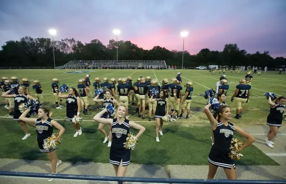 Cheerleader e giocatori di football americano della Hayden Catholic High School sul campo sportivo al tramonto.