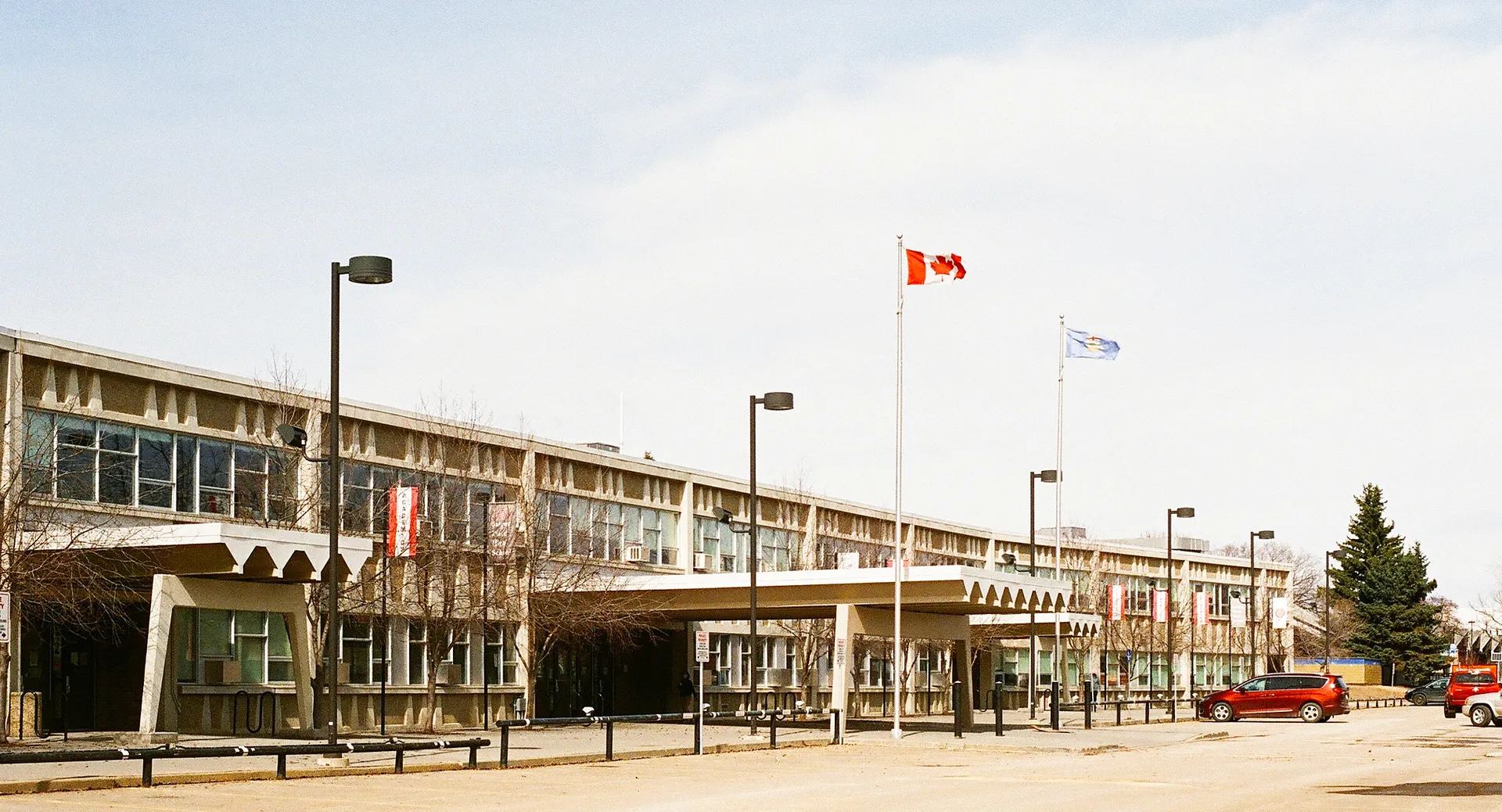 L'edificio a più piani della Jasper Place High School con una serie di bandiere in primo piano e un parcheggio con alberi sullo sfondo.