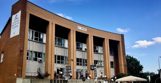 L'edificio in mattoni a più piani con ampie finestre e facciata curva della Beurling Academy si staglia contro un cielo limpido.