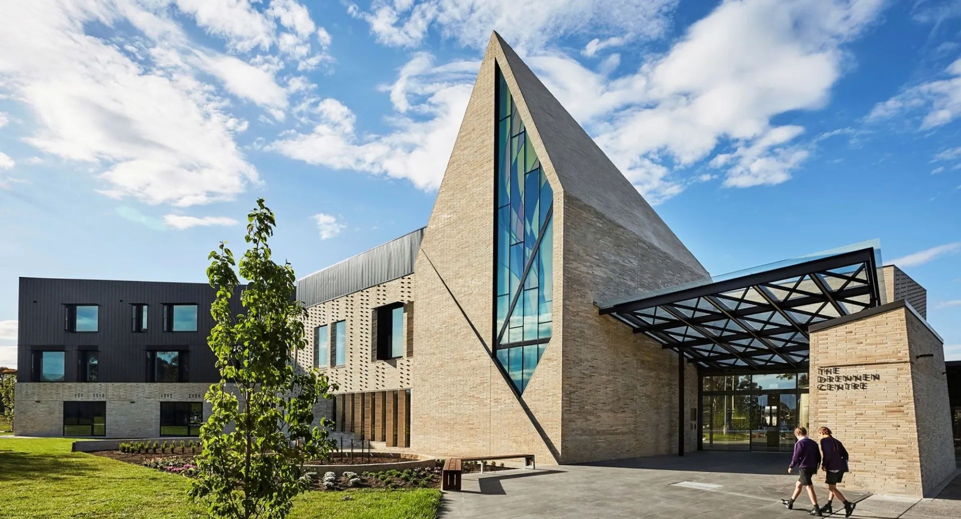 Un edificio moderno con facciata in vetro si trova nel campus del Wesley College, circondato da aree verdi e alberi.
