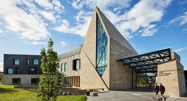 Un edificio moderno con facciata in vetro si trova nel campus del Wesley College, circondato da aree verdi e alberi.