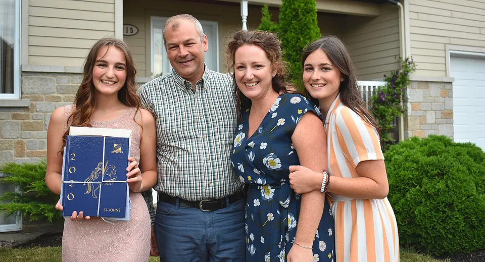 Una famiglia con due adulti e due giovani donne si trova davanti a un edificio residenziale sul terreno della St. Johns High School.