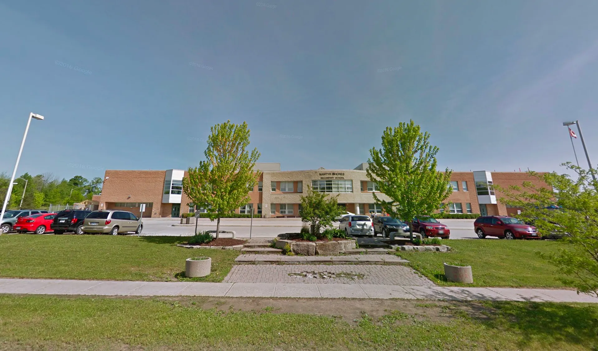 L'edificio in mattoni a più piani della Nantyr Shores Secondary School, con un'area verde e alberi in primo piano, è circondato da un parcheggio pavimentato.