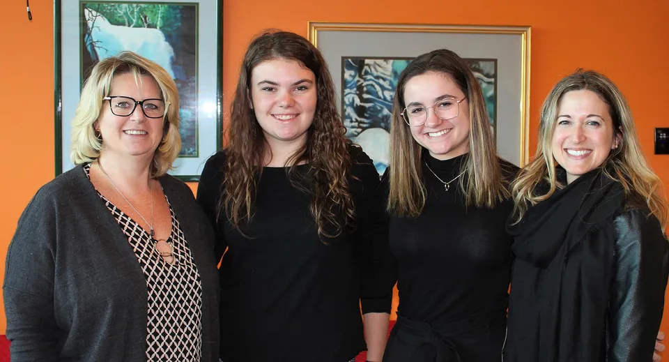 Quattro donne posano davanti a una parete arancione nel campus della St. Johns High School.