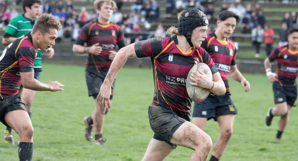 Un gruppo di giocatori di rugby del Kapiti College disputa una partita intensa su un campo d'erba con spettatori sullo sfondo.