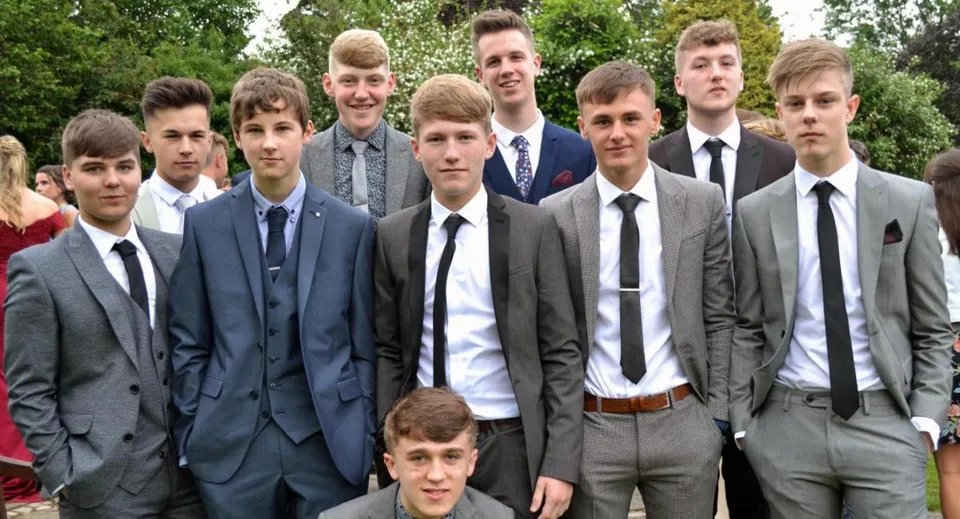 Un gruppo di studenti del Dulwich College in abito formale all'aperto, davanti ad alberi e aree verdi.