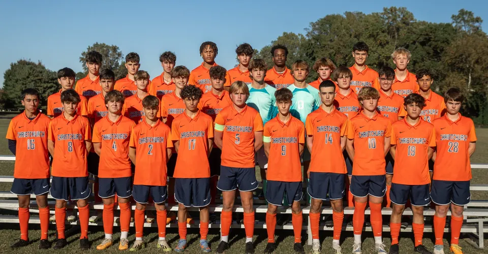 Un gruppo di giovani calciatrici e calciatori della Christchurch School si trova insieme su un campo con alberi e cielo azzurro.