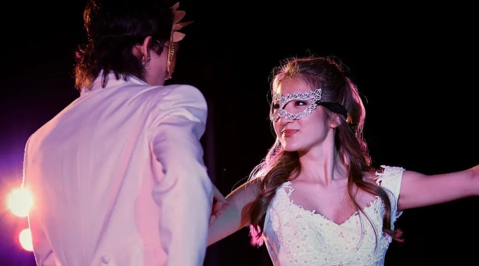 Una donna indossa un vestito bianco e una maschera a un evento della Iolani School con un'illuminazione di sfondo colorata.