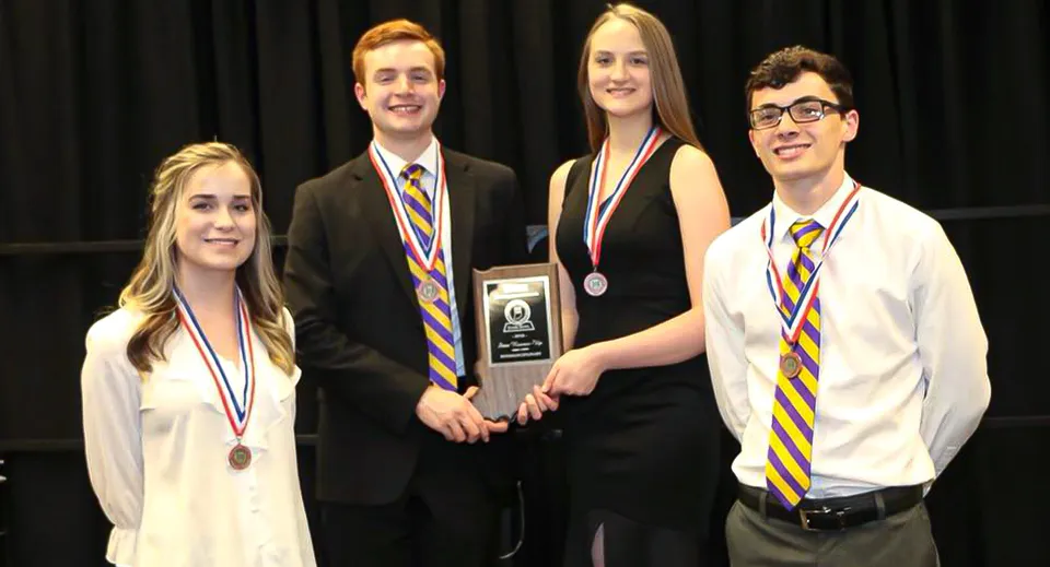 Quattro studenti della Scottsburg High School sono in piedi insieme su un palco con premi e medaglie in mano.