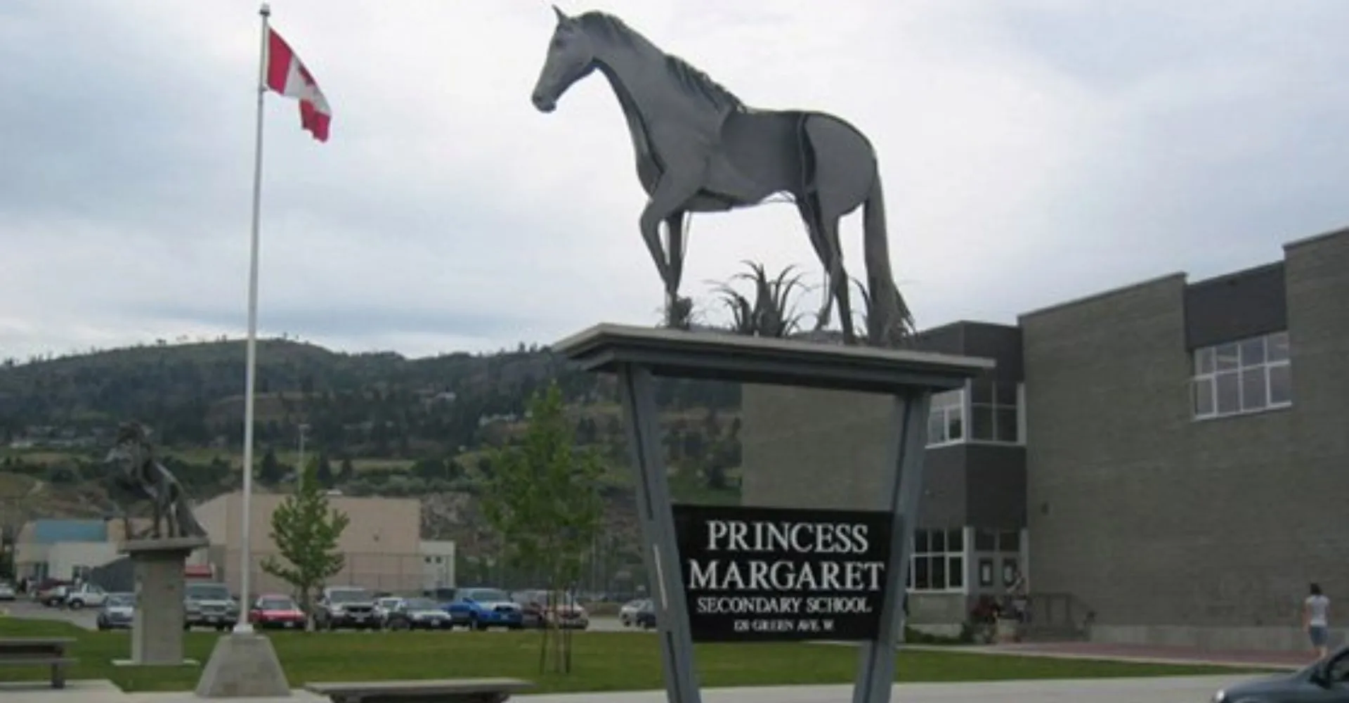 Una grande statua di un cavallo si trova nel terreno della Princess Margaret Secondary School davanti a un edificio e a una bandiera canadese.