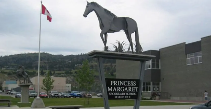 Una grande statua di un cavallo si trova nel terreno della Princess Margaret Secondary School davanti a un edificio e a una bandiera canadese.