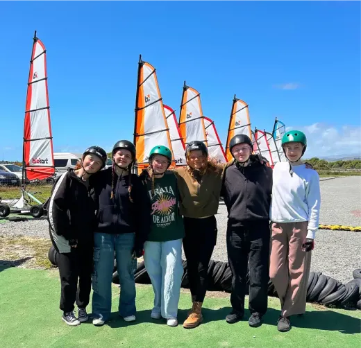 Jugendliche mit Helmen vor Blokart-Segeln unter blauem Himmel in Neuseeland
