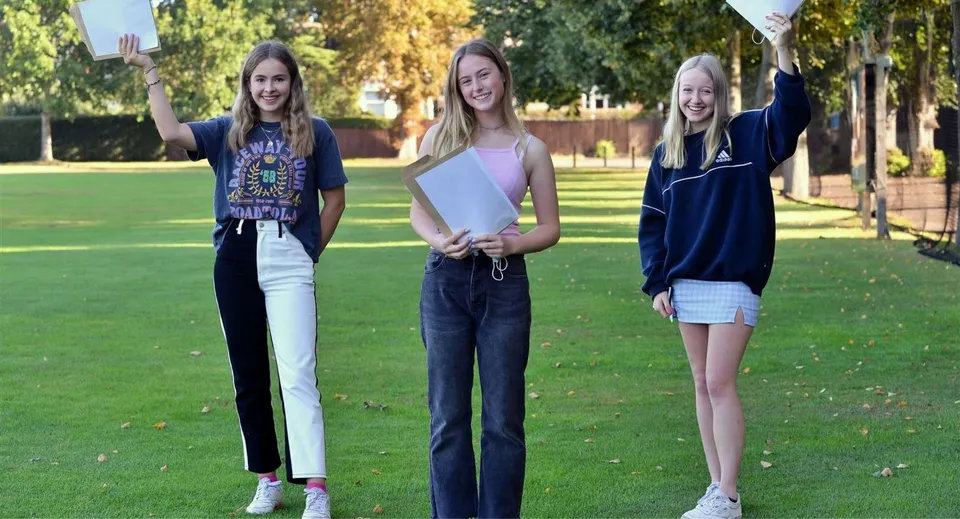 Tre studentesse della Ipswich School si trovano su un prato all'interno di un parco e sorridono alla fotocamera.