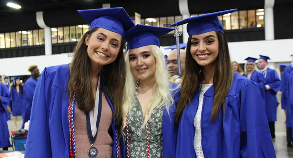 Tre studentesse della Wellington Heights Secondary School festeggiano il diploma in toge e tocchi blu.