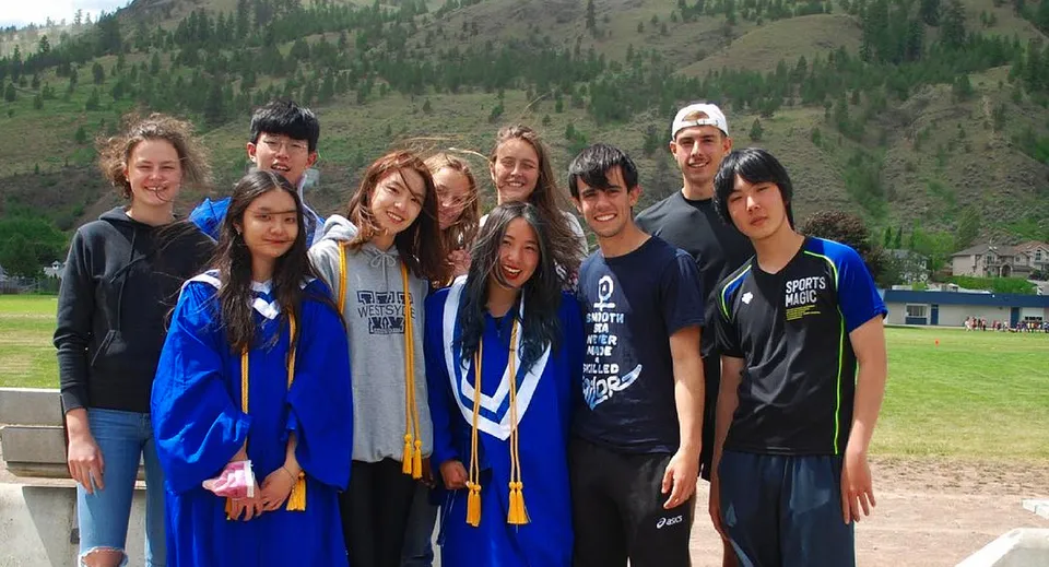 Un gruppo di studenti della Westsyde Secondary School posa davanti a un panorama montano boscoso.