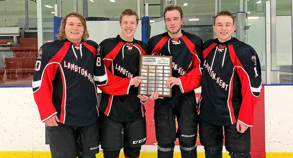 Quattro studenti in divisa da hockey tengono un trofeo davanti al campo da hockey sul campus della Lambton Kent Composite School.