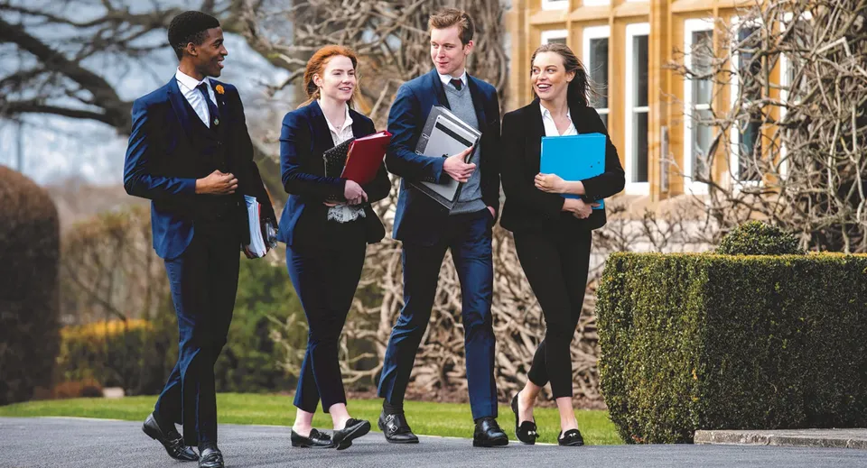 Un gruppo di quattro persone cammina su un viale alberato all'interno del campus della Millfield School.