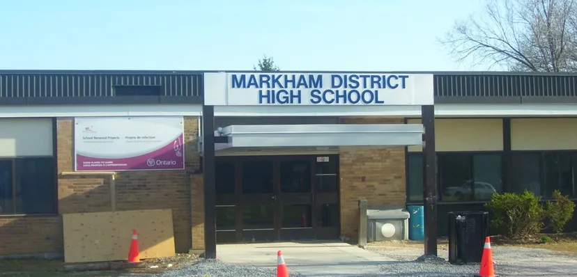 L'edificio in mattoni della Markham District High School con una vistosa insegna si trova davanti ad alberi e a un cielo limpido.