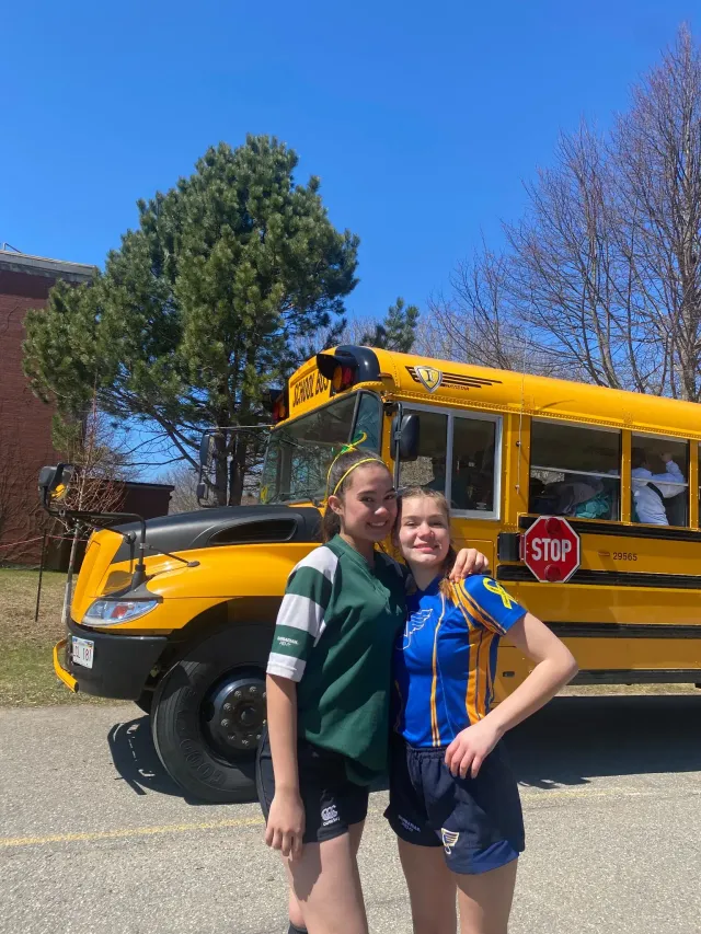 Due studentesse in maglia da rugby abbracciate davanti a uno scuolabus giallo in Canada