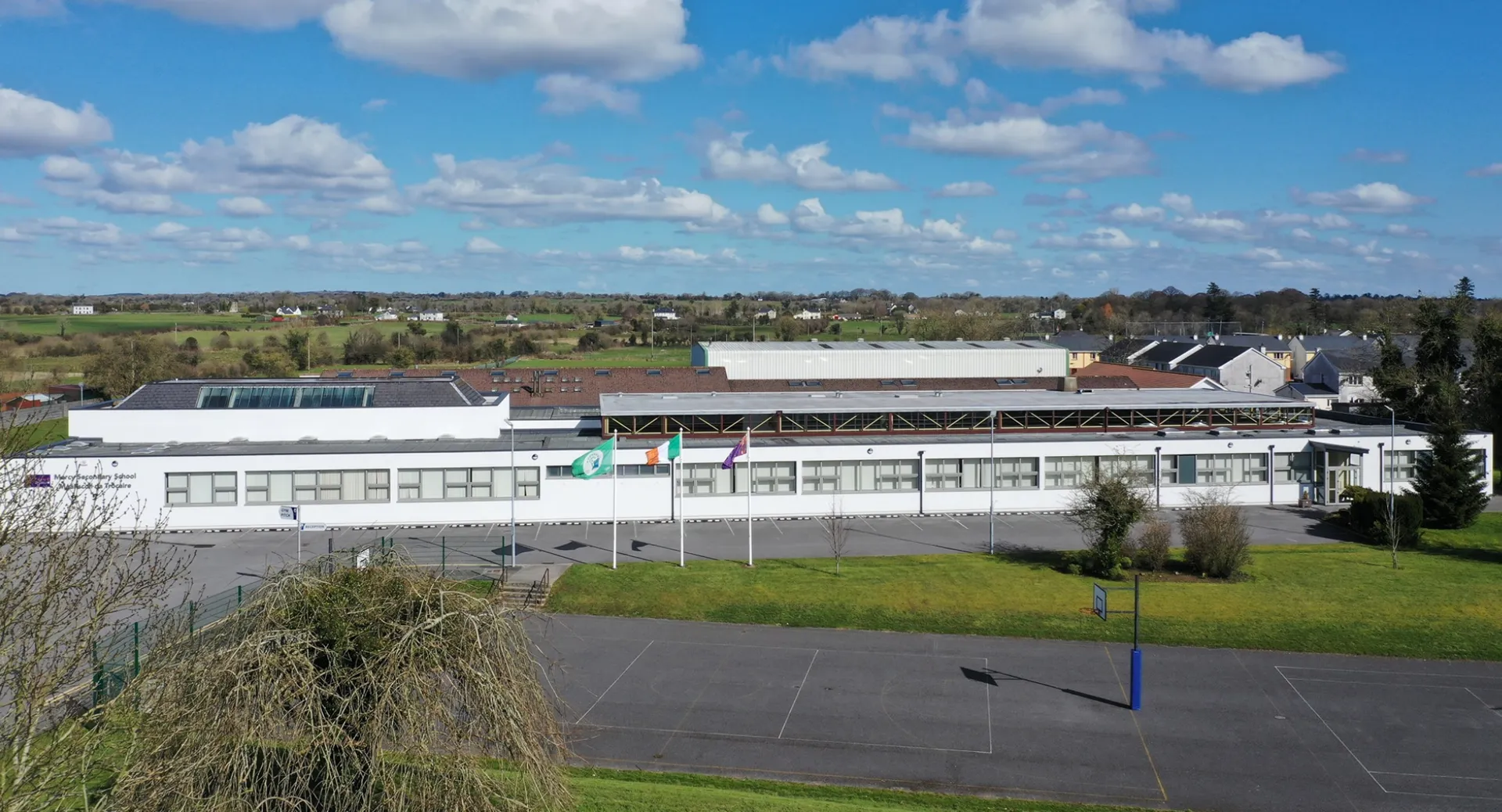 L'edificio industriale bianco nel terreno della Mercy Secondary School Ballymahon sotto un cielo blu con nuvole.