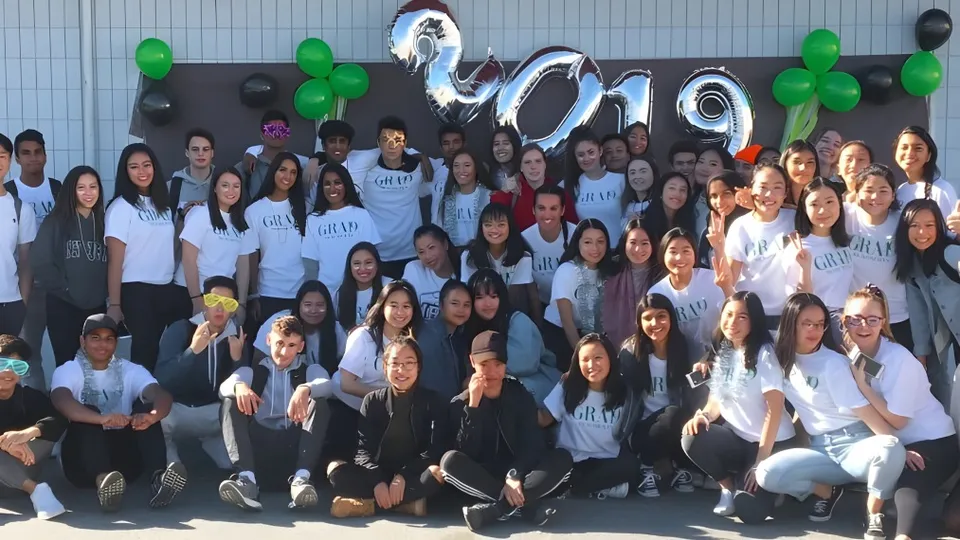 Un gruppo di studenti e studentesse è in piedi davanti a uno striscione con l'anno 2019 nel campus della Hugh McRoberts Secondary School.