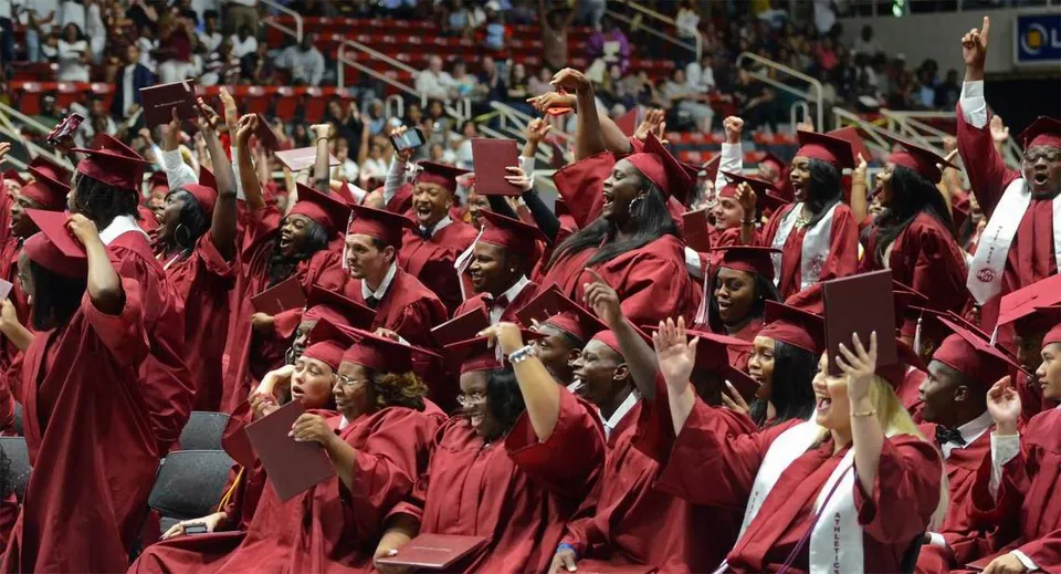 I diplomati e le diplomate delle Charlotte-Mecklenburg Schools festeggiano la loro cerimonia di diploma in toga rossa davanti al palco e al pubblico.