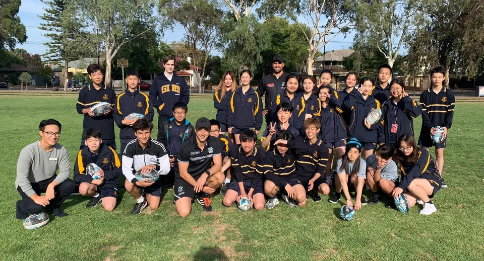 La squadra sportiva della Glenunga International High School posa insieme su un campo da gioco erboso con alberi sullo sfondo.