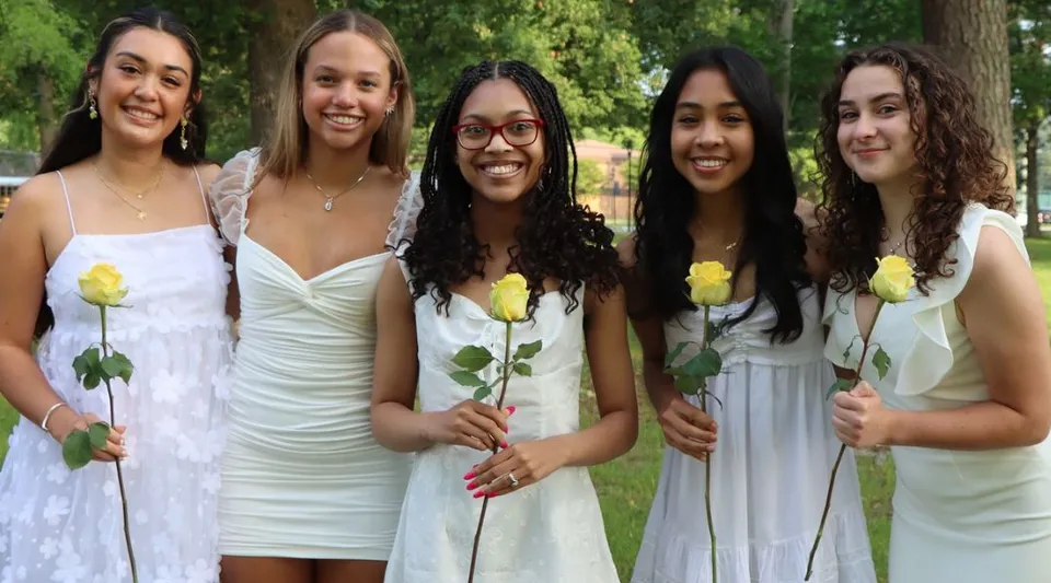 Cinque studentesse della Nansemond-Suffolk Academy sono in piedi con rose gialle in un'area verde all'aperto.