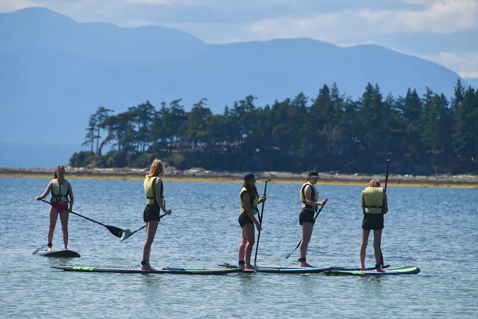 Studenti della Mark R. Isfeld Secondary School mentre fanno paddleboarding su un lago circondato da boschi e montagne.