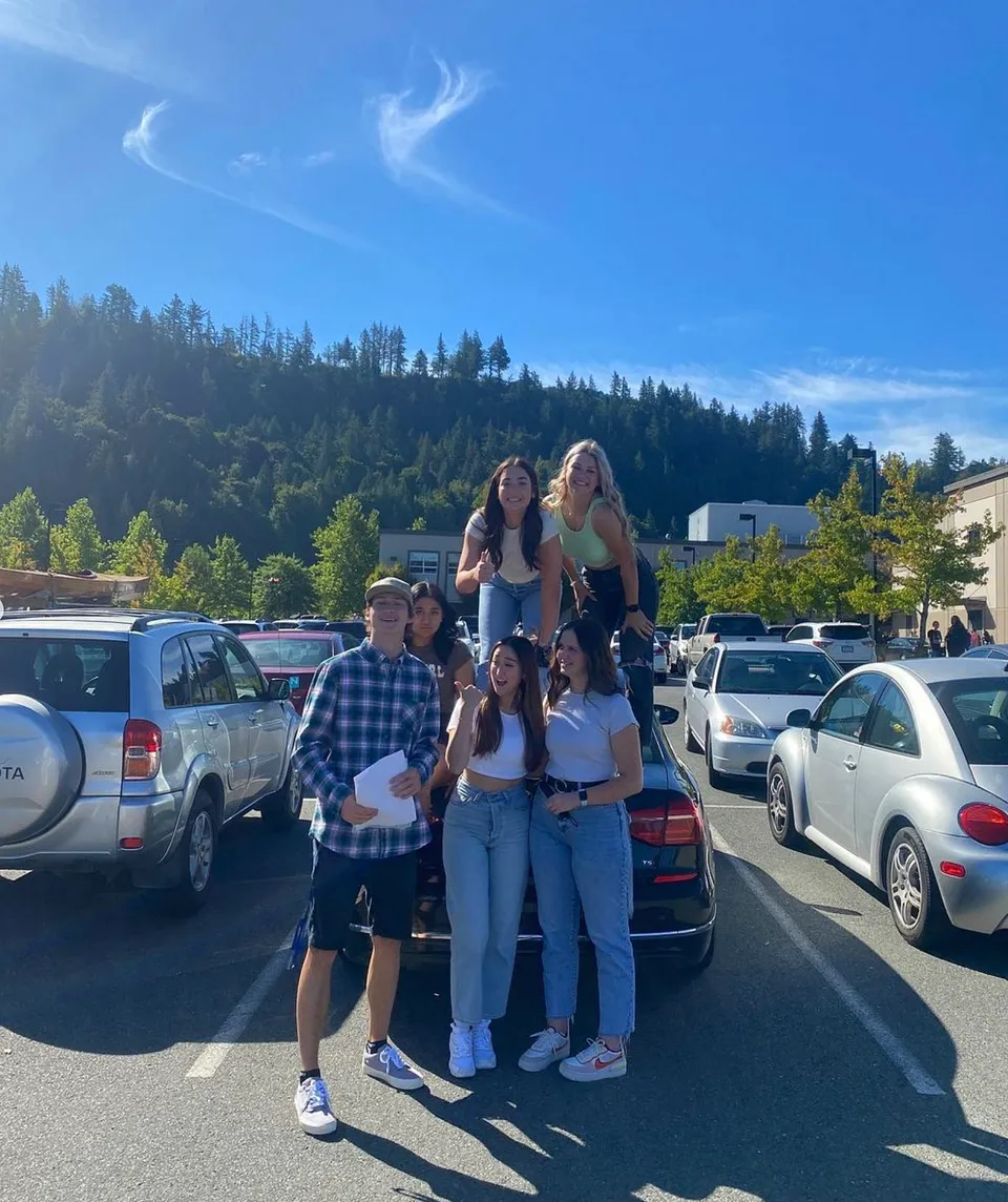 Un gruppo di studenti si trova nel campus della G.W. Graham Secondary School davanti a montagne e alberi.