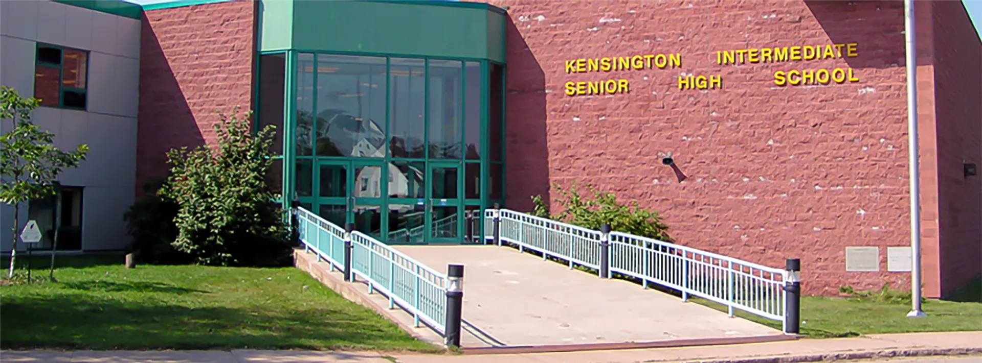 L'edificio scolastico moderno della Kensington Intermediate Senior High School con un ingresso in vetro verde e una parete in mattoni rossi all'esterno.