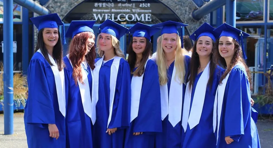 Un gruppo di studentesse della Lambrick Park Secondary School festeggia il diploma in toga blu davanti a un cartello di benvenuto.