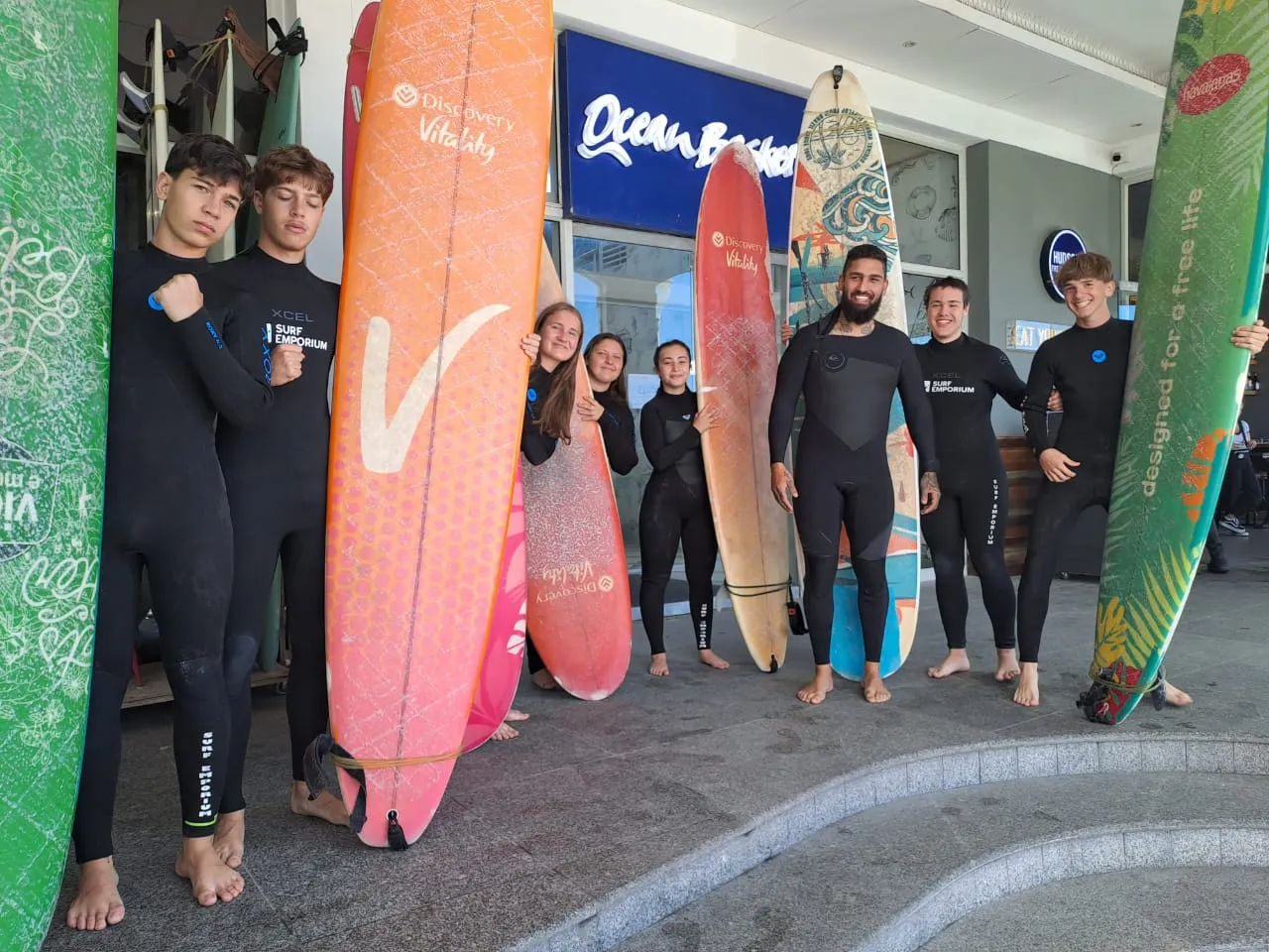 Gruppo di studenti in muta con le tavole da surf davanti a un surf shop in Sudafrica