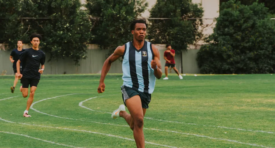 Uno studente o una studentessa del Hamilton Secondary College corre su un campo verde durante un'attività sportiva.
