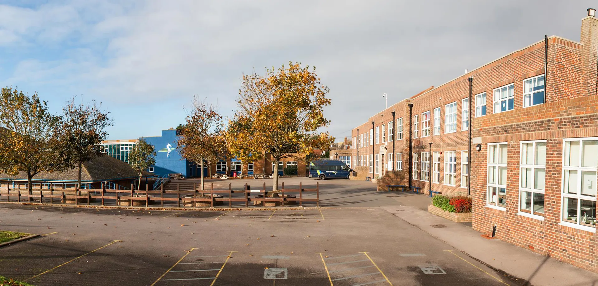 L'edificio in mattoni della Seaford Head School con un cortile e alberi d'autunno dai colori vivaci sotto un cielo nuvoloso.